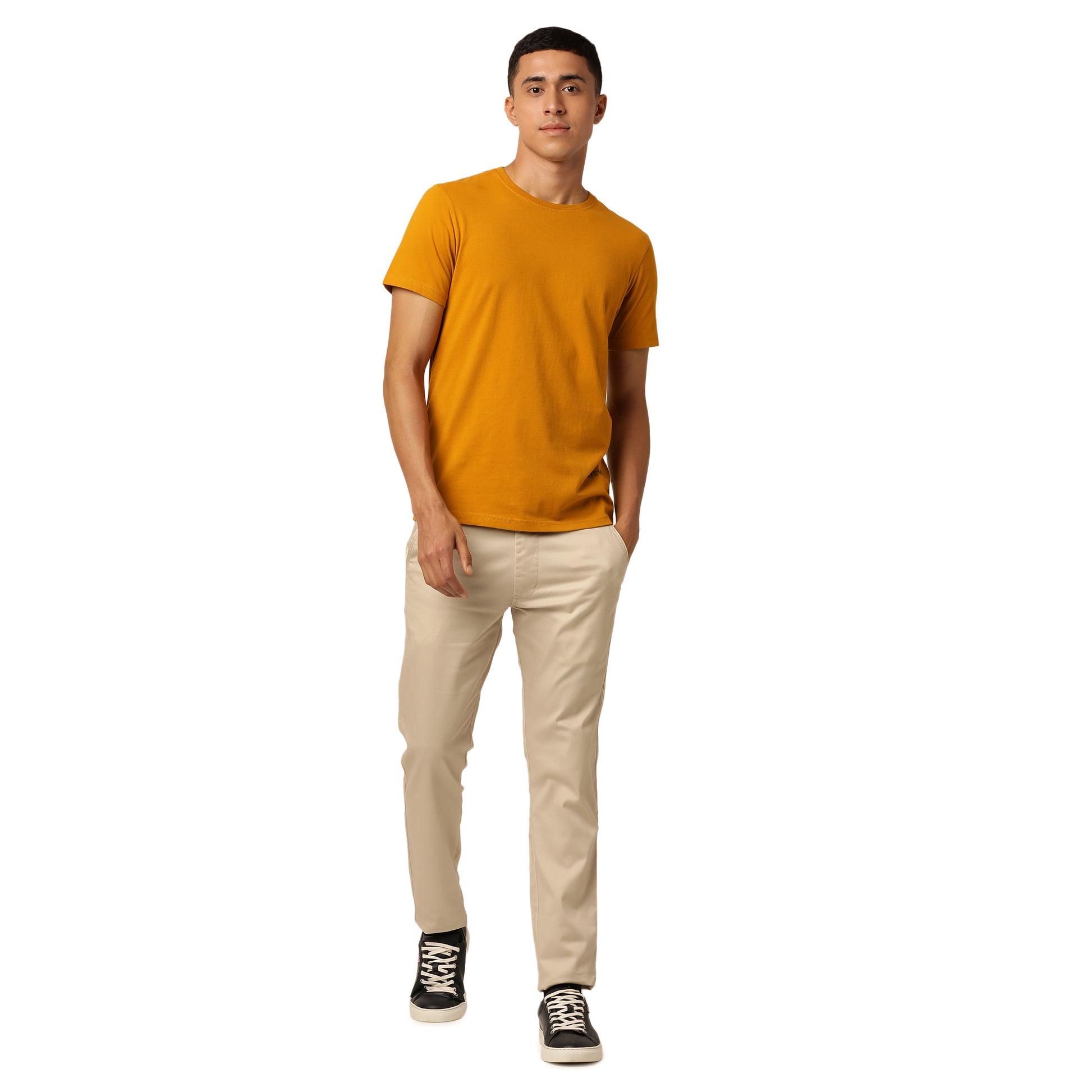 A person stands against a white background, wearing a mustard yellow Northmist Amity Combo Pack: Organic Crew Neck T-shirt, beige pants, and stylish black high-top sneakers. The individual has one hand in their pocket and looks directly at the camera with a neutral expression.